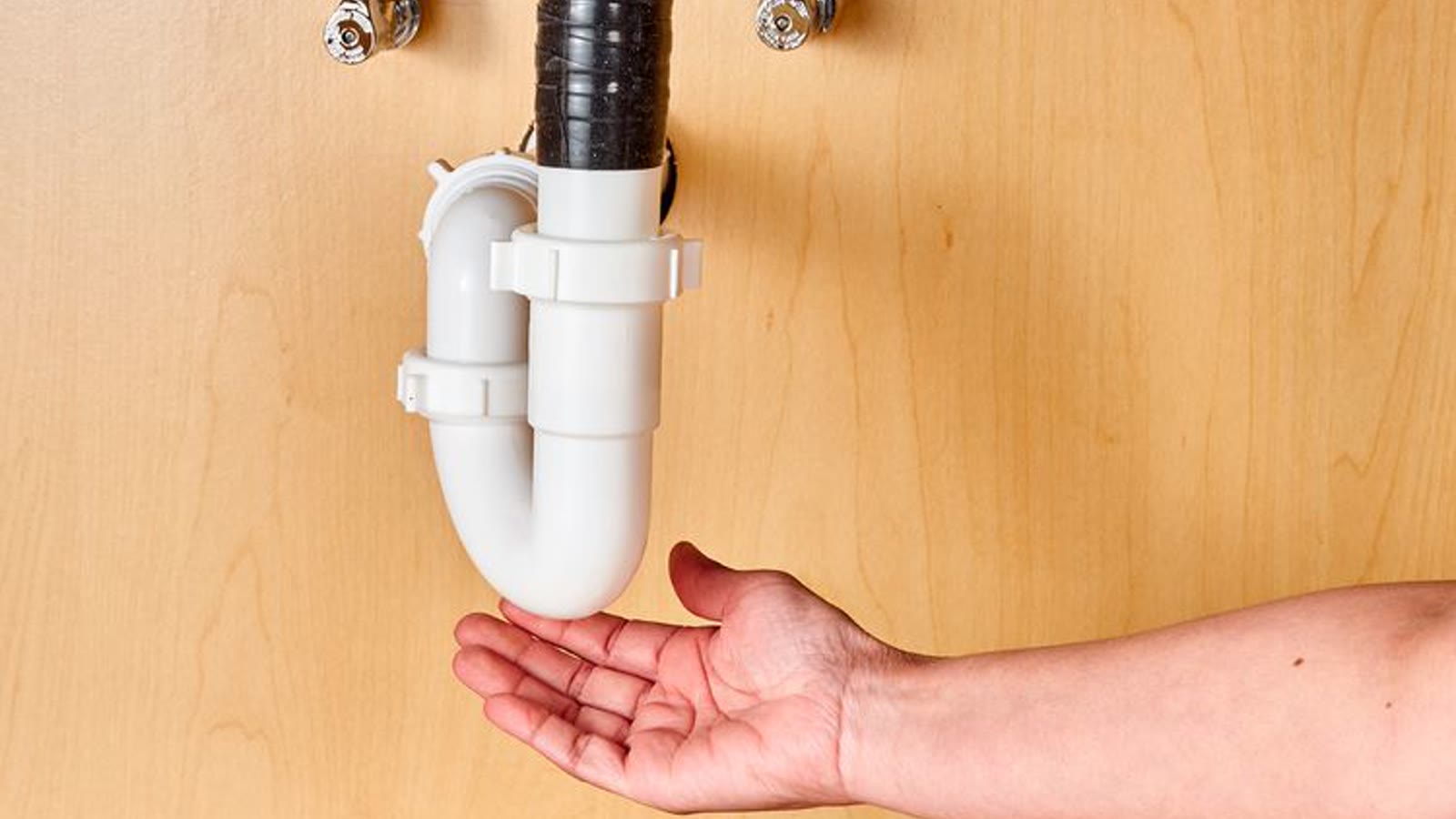 Hand checking the drain connection beneath a kitchen sink